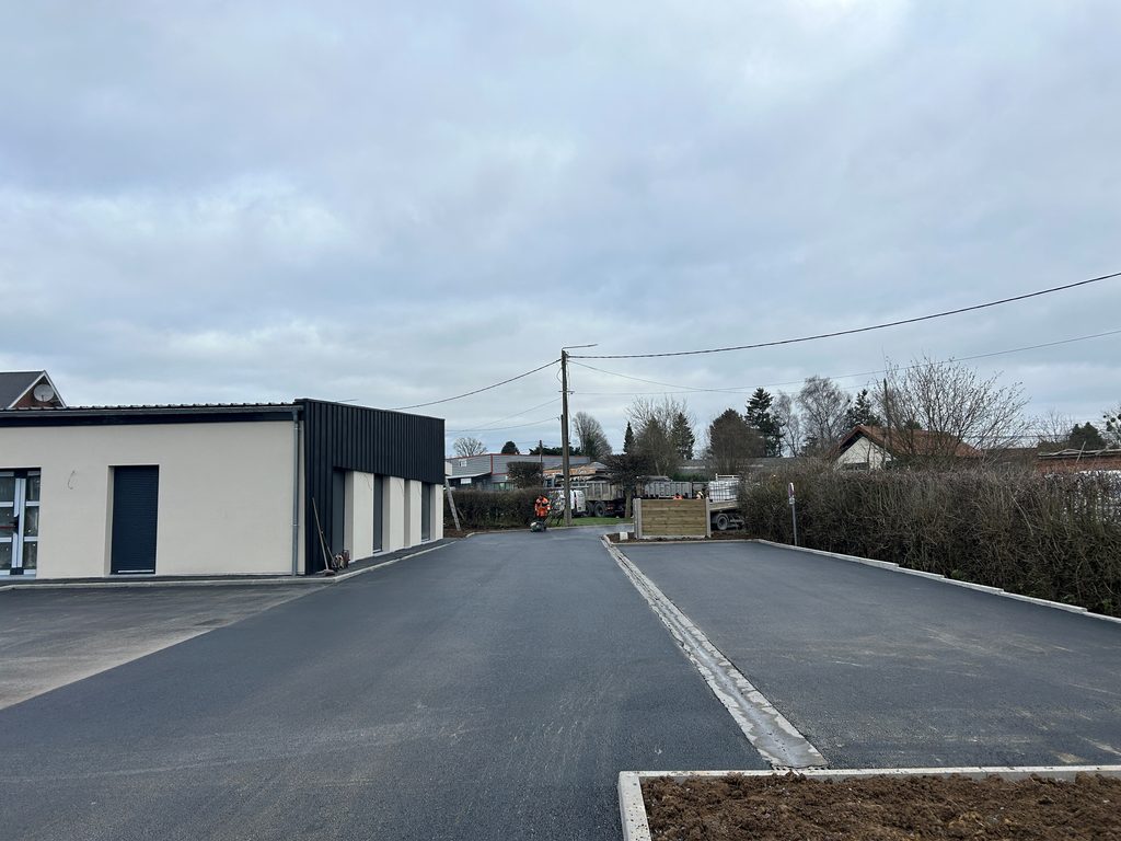 Parking terminé en enrobé noir avec bordures béton et caniveau, près d’un bâtiment de maison médicale